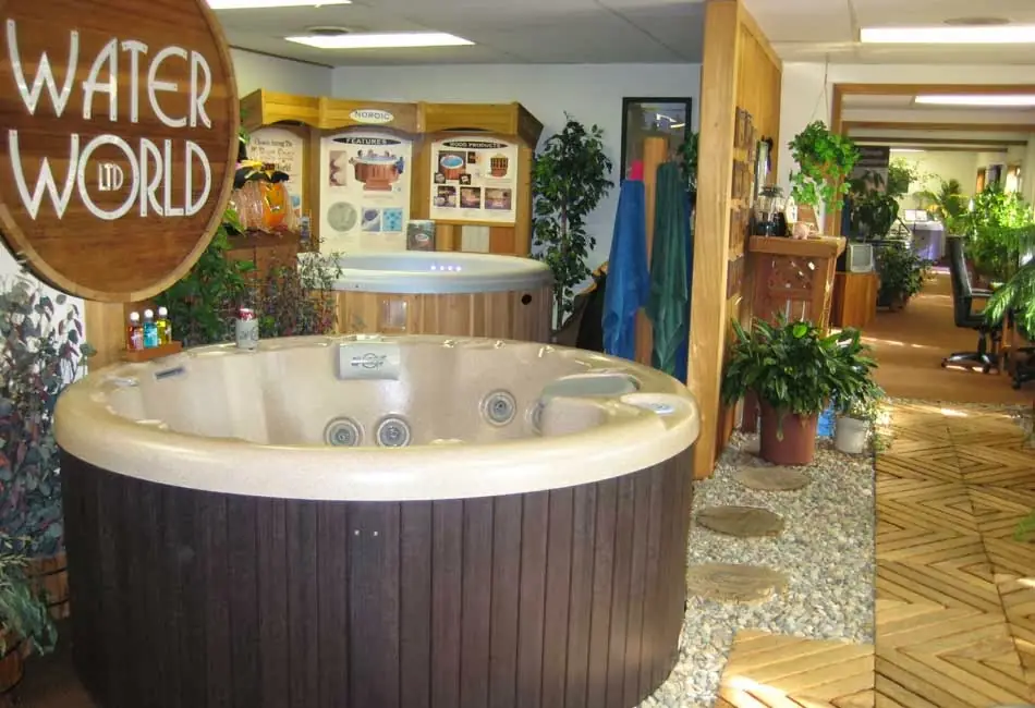 Round hot tub with a dark wood skirt under the cedar sign, showroom behind
